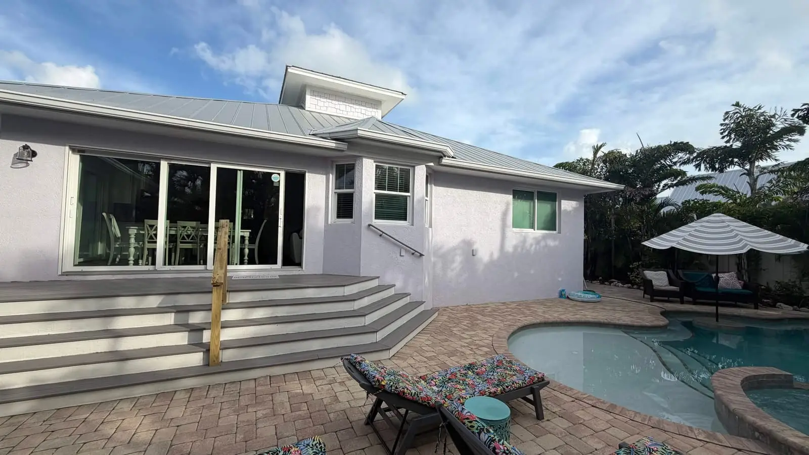 Wide steps down from a covered lanai to a paver patio and pool