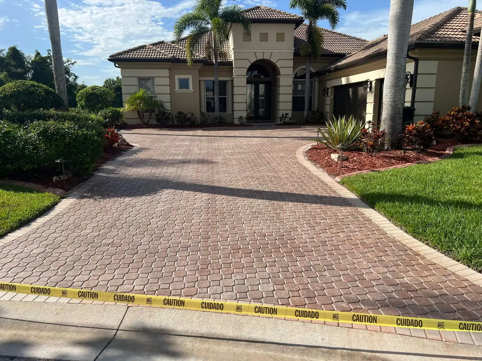 A curved brick-paver driveway between landscaped beds, leading up to a stucco home