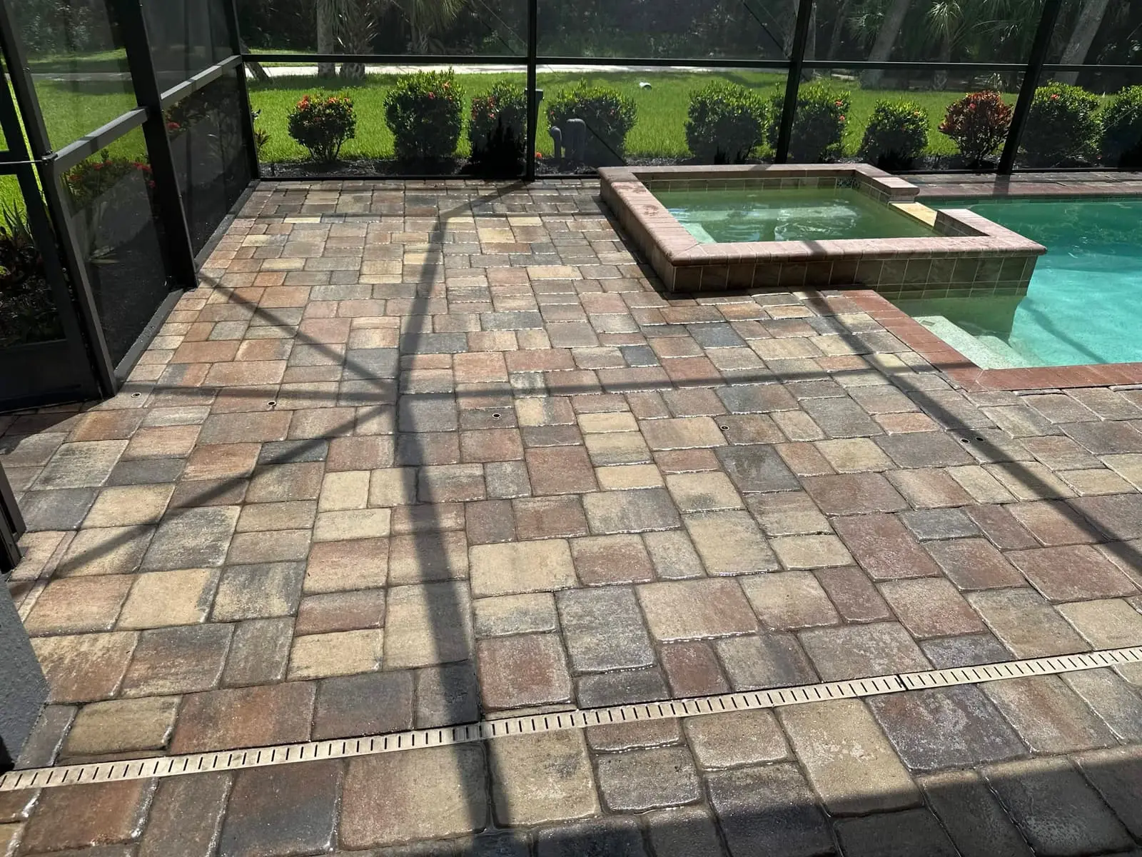 A paver pool deck around a raised spa, inside a screen enclosure