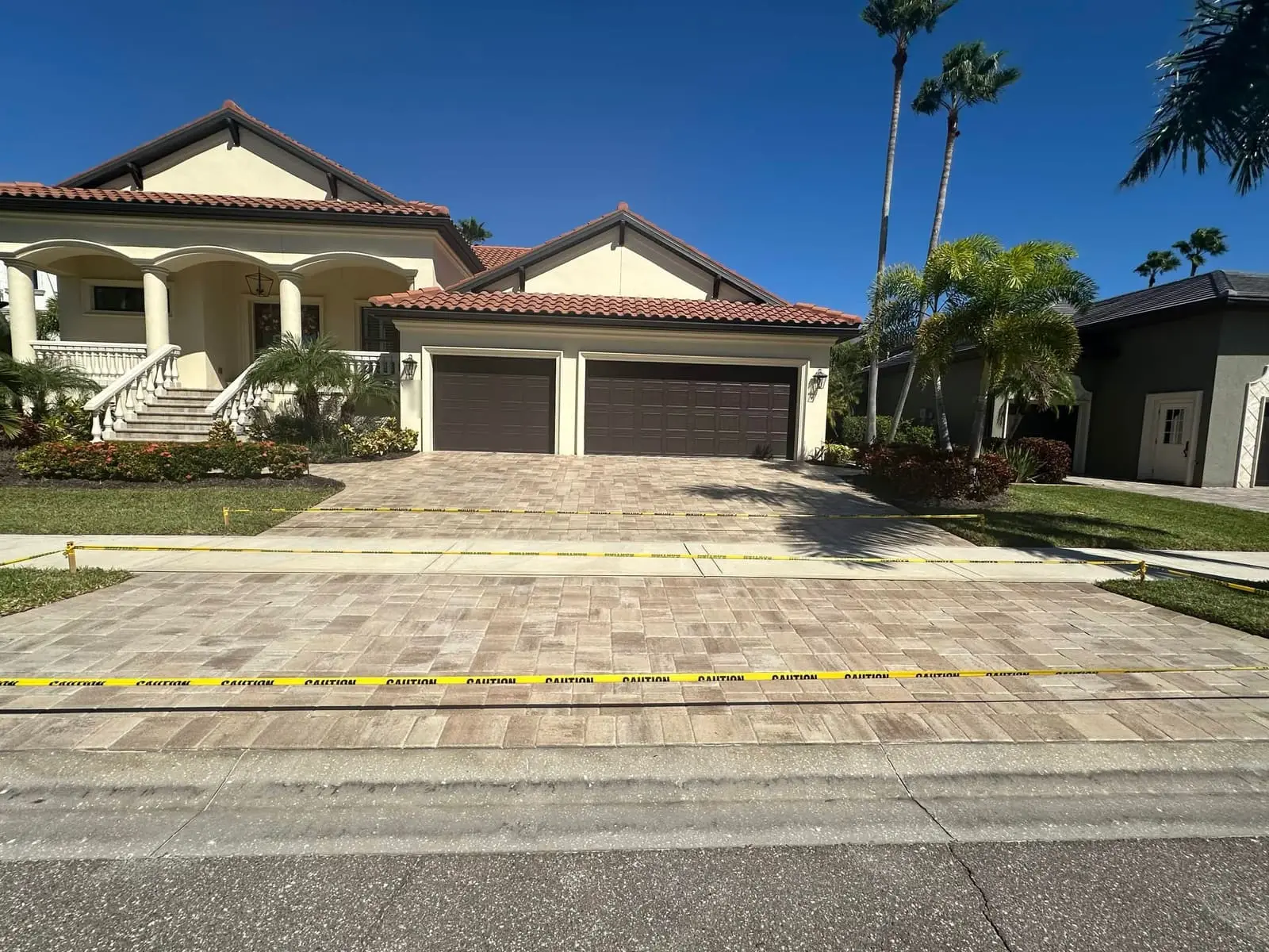 A paver driveway in front of a three-car garage, with caution tape across it