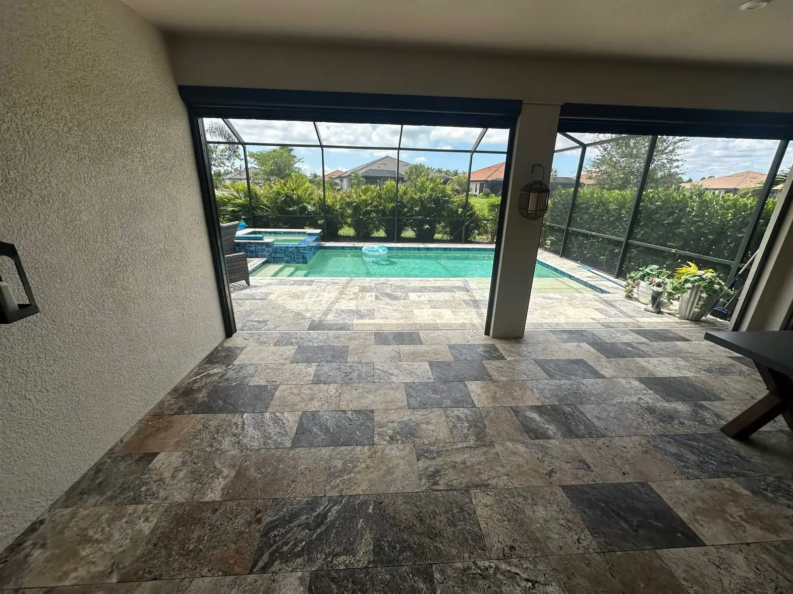 A covered travertine lanai opening onto a pool and screen enclosure