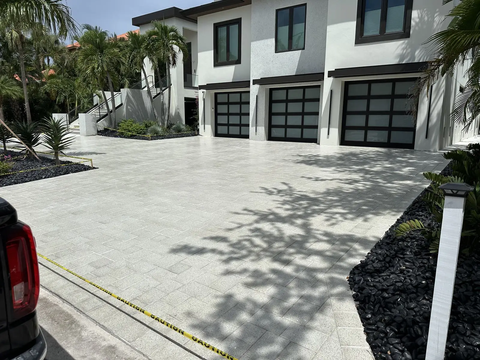 A wide white paver driveway in front of a modern home with three glass garage doors