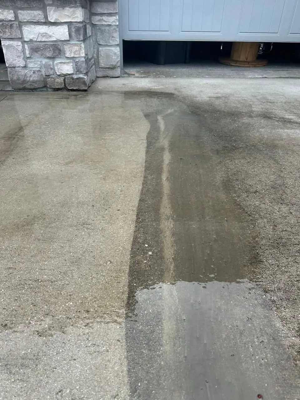 A clean stripe washed through a stained concrete driveway, the difference side by side