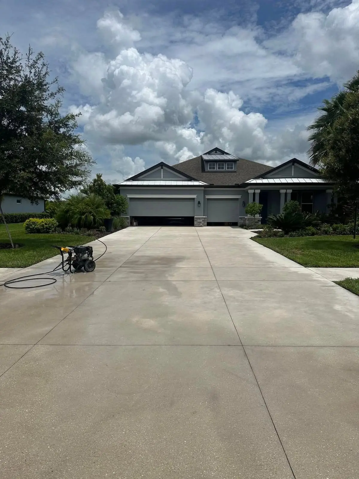A long concrete driveway after washing, with the pressure washer still on it